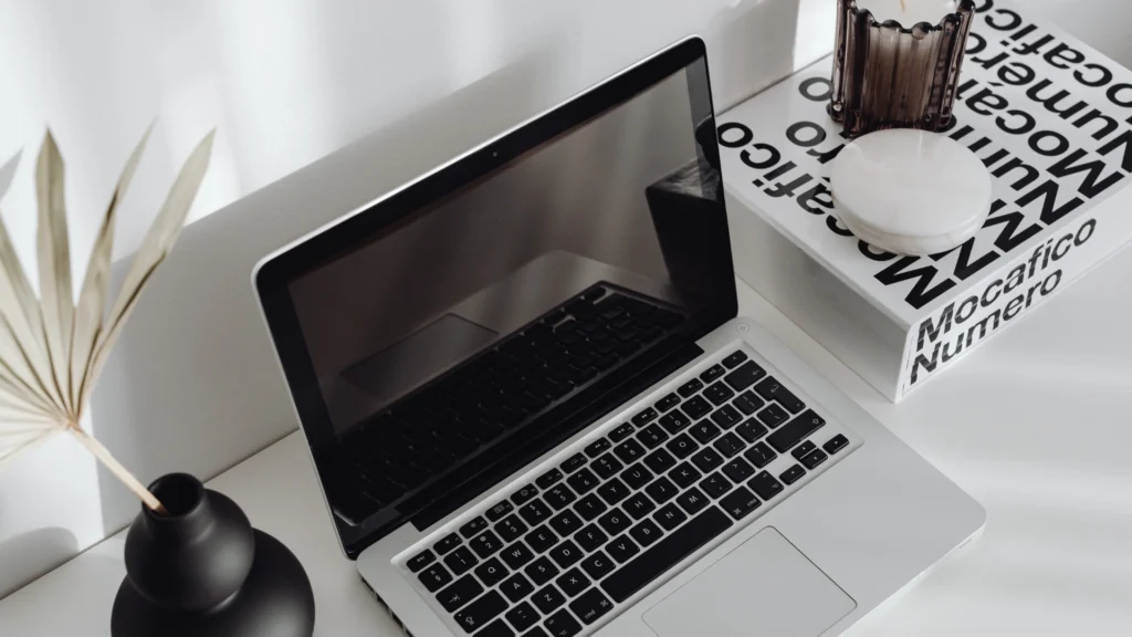 A cozy workspace in Calicut, Kerala, featuring a black laptop, a flower vase, a book, and a candle, symbolizing the creativity and focus of a digital marketing strategist.